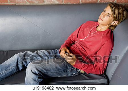 Stock Image - Teenage boy lying on a seat listening to music on mp3. Fotosearch