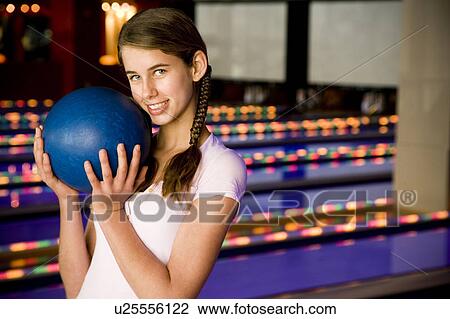 Stock Image - Teenage girl in a bowling alley, holding a blue bowling ball. Fotosearch