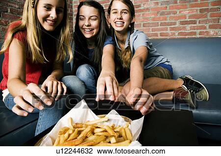 Stock Image - Three teenage girls sharing a plate of chips. Fotosearch