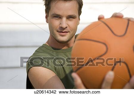 Stock Image - Man in a green vest holding a basketball.. Fotosearch