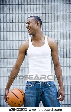 Stock Image - Portrait of a smiling young African American man holding a basketball. . Fotosearch