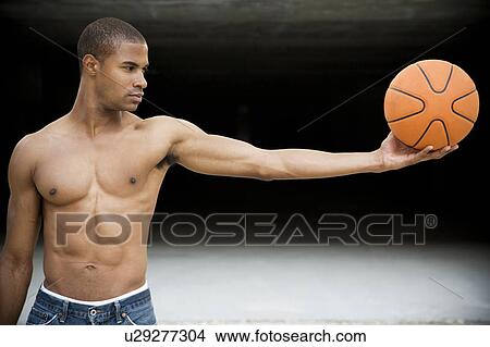 Portrait of a young African American man holding a basketball in outstretched arms View Large Photo Image Picture - Portrait of a young African American man holding a basketball in outstretched arms. Fotosearch