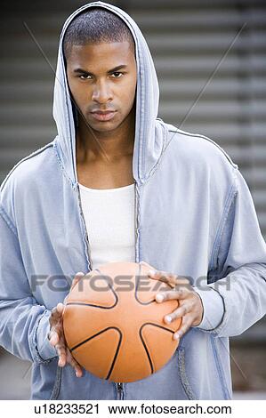 Portrait of a young African American man in a grey hooded top holding a basketball. View Large Photo Image Stock Image - Portrait of a young African American man in a grey hooded top holding a basketball. . Fotosearch