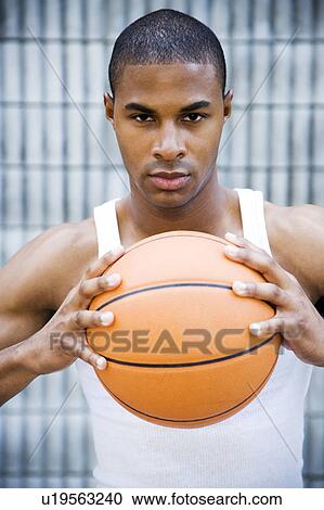 Stock Image - Portrait of a young African American man holding a basketball. . Fotosearch