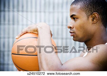 Stock Image - Portrait of a young African American man holding a basketball. . Fotosearch