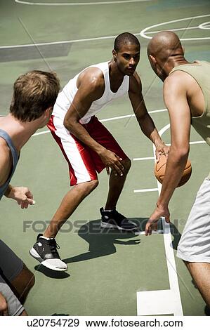 Stock Photo - Three men playing basketball on an outdoor court . Fotosearch
