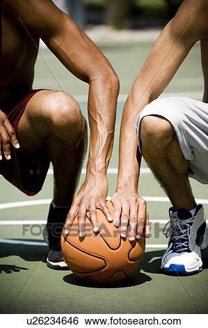 Stock Photograph - Two African American kneeling side by side on an urban basketball court, close up. Fotosearch