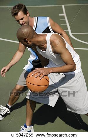 Stock Photography - Two men playing basketball on a green urban outside court. Fotosearch