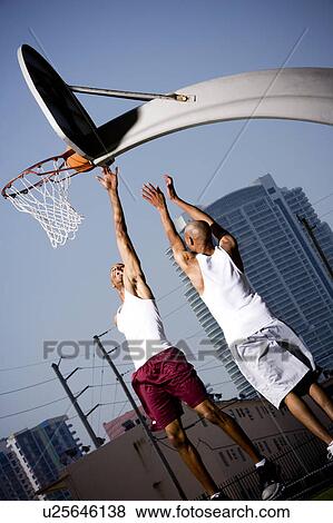 Stock Photo - Two Young African American man jumping with a basketball on an urban basketball court. Fotosearch