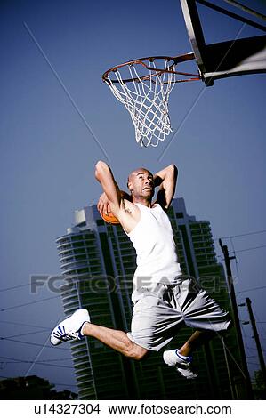 Picture - Young African American man jumping with a basketball on an urban basketball court. Fotosearch