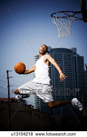 Stock Photo - Young African American man jumping with a basketball on an urban basketball court. Fotosearch