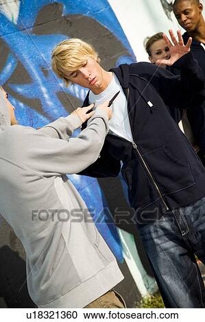 Confrontation between two young men and a group of friends in front of a graffiti covered wall View Large Photo Image Stock Image - Confrontation between two young men and a group of friends in front of a graffiti covered wall . Fotosearch