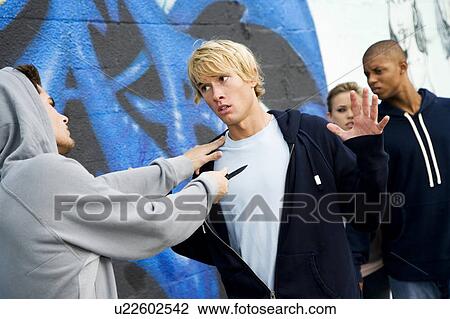 Stock Image - Confrontation between two young men and a group of friends in front of a graffiti covered wall . Fotosearch