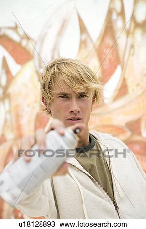 Portrait of a young man holding a spray can in front of a wall covered in graffiti View Large Photo Image Stock Image - Portrait of a young man holding a spray can in front of a wall covered in graffiti . Fotosearch