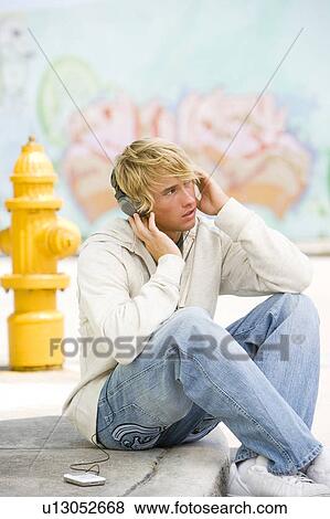 Portrait of a young man listening to music in front of a graffiti covered wall View Large Photo Image Stock Photo - Portrait of a young man listening to music in front of a graffiti covered wall. Fotosearch