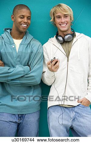 Picture - Two young men looking at an MP3 Player leaning against a green painted wall . Fotosearch