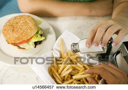 Stock Photo - Close up of a girl putting salt on her fries. Fotosearch