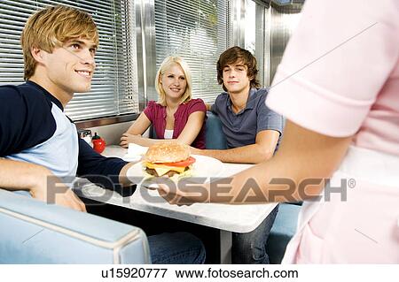 Diner waitress serving food to teenage customers in a diner View Large Photo Image Stock Photo - Diner waitress serving food to teenage customers in a diner. Fotosearch