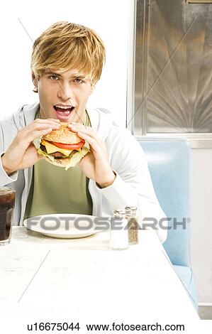 Teenage boy eating a large hamburger in a diner View Large Photo Image Picture - Teenage boy eating a large hamburger in a diner . Fotosearch
