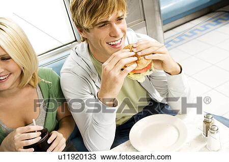 Stock Image - Teenage boy eating a large hamburger in a diner . Fotosearch