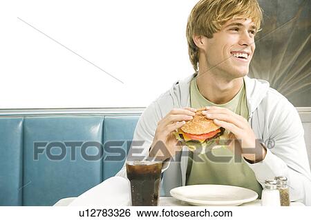 Stock Photograph - Teenage boy eating a large hamburger in a diner . Fotosearch