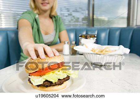 Picture - Teenage girl reaching for a hamburger in a diner . Fotosearch