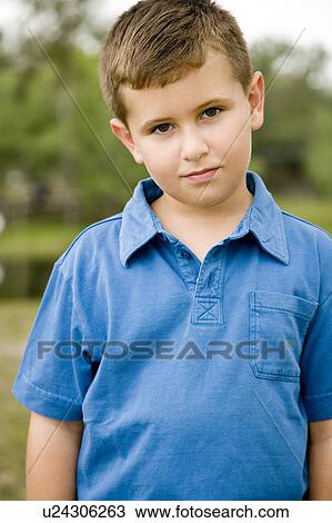 Stock Image - boy standing in park wearing blue polo shirt. Fotosearch