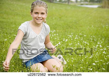Stock Image - girl sitting on grass picking flowers. Fotosearch