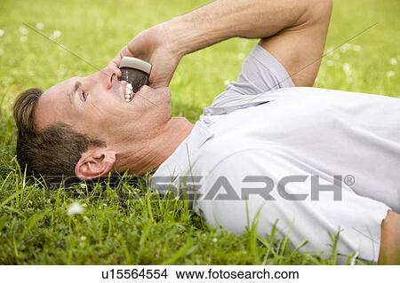 man lying on the grass talking on mobile phone View Large Photo Image Picture - man lying on the grass talking on mobile phone. Fotosearch