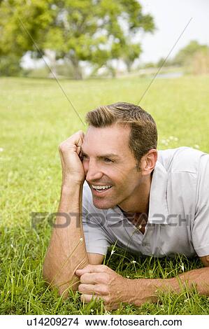 Picture - portrait man lying on grass leaning on elbow. Fotosearch