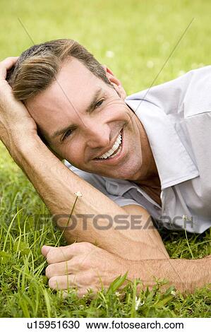 Stock Image - portrait man lying on grass leaning on elbow. Fotosearch