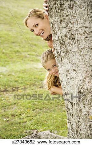 Stock Image - woman playing hide and seek behind a tree. Fotosearch