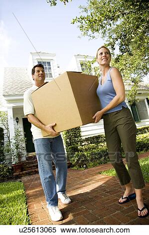 Couple moving into their new home, carrying a packing box View Large Photo Image Stock Photography - Couple moving into their new home, carrying a packing box. Fotosearch