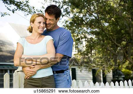 Stock Image - Couple standing by the garden fence outside their new home. Fotosearch