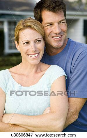 Stock Photo - Couple standing by the garden fence outside their new home. Fotosearch