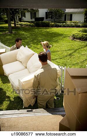 Stock Photo - Woman directing removal men carrying sofa into new home. Fotosearch