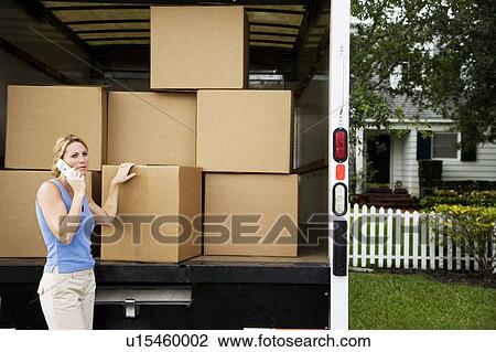 Stock Image - Woman moving home, standing beside removal van and talking on her mobile phone. Fotosearch