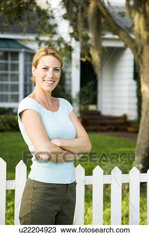 Woman standing by the garden fence outside her new home View Large Photo Image Stock Image - Woman standing by the garden fence outside her new home. Fotosearch