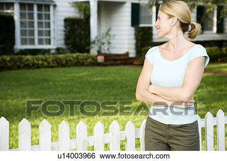 Woman standing by the garden fence outside her new home View Large Photo Image Stock Photograph - Woman standing by the garden fence outside her new home. Fotosearch