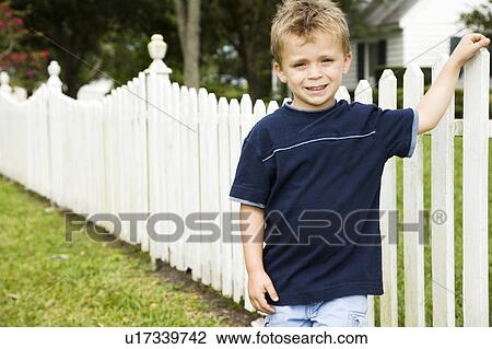 Stock Image - little boy standing by picket fence. Fotosearch