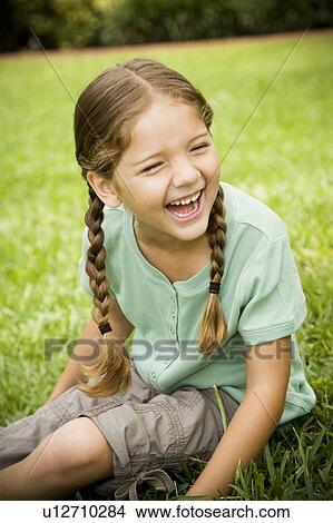 Picture - little girl sitting on the grass laughing. Fotosearch