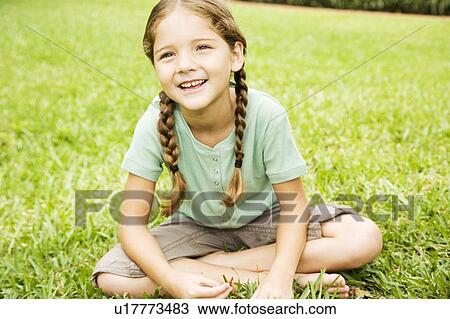 Stock Image - little girl with pigtails sitting cross legged on the grass. Fotosearch