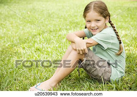 Stock Image - little girl with pigtails sitting on the grass. Fotosearch