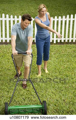 Stock Photo - man mowing the lawn, wife pointing at grass. Fotosearch