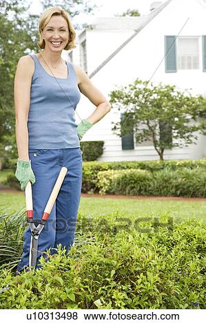 Stock Photo - woman standing in the garden holding shears. Fotosearch