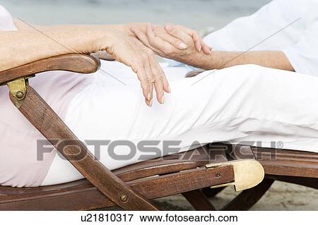 Stock Photo - Close up of a senior couple relaxing in wooden steamer chairs at the beach . Fotosearch