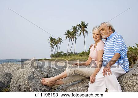 Portrait of a couple sitting on rocks on a beach View Large Photo Image Stock Image - Portrait of a couple sitting on rocks on a beach. Fotosearch