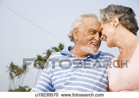 Stock Image - Portrait of a romantic senior couple sitting on a beach. Fotosearch