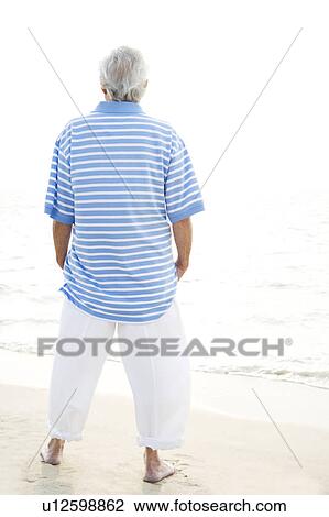 Stock Image - Portrait of a senior man standing on a beach looking out to sea. Fotosearch
