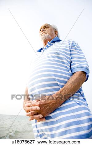 Portrait of a senior man standing on a beach looking thoughtful View Large Photo Image Stock Photo - Portrait of a senior man standing on a beach looking thoughtful. Fotosearch